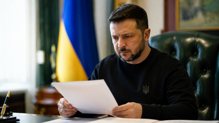 Владимир Зеленский читает документы по делу Тимура Миндича на фоне флага Украины.
