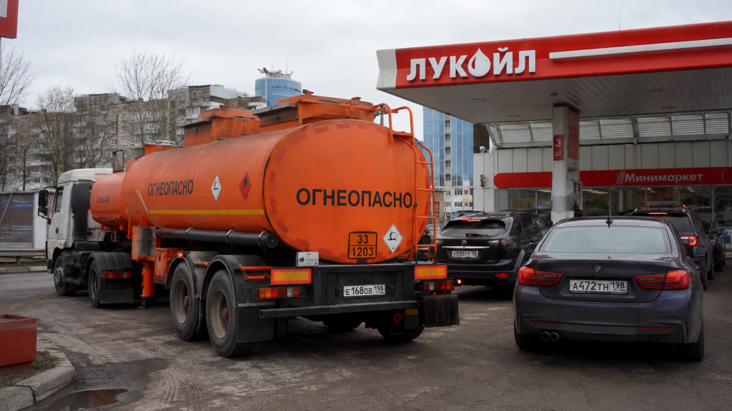 Бензовоз с российскими номерами доставляет топливо на АЗС, рядом стоят автомобили в ожидании заправки.